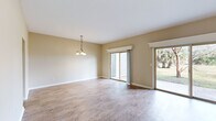 This two-story, 3-bedroom, 3-bathroom home offers a well-organized layout across two floors, combining functional living spaces with classic design details. The main floor features a generous living room with light wood-style flooring, neutral warm-toned walls, and a striking brick fireplace with a raised hearth and white decorative mantle that serves as a central focal point. Two sliding glass doors flood the space with natural light and provide direct access to a patio overlooking a spacious, open yard with mature trees. A staircase from the living area leads to the upper floor. The kitchen is equipped with warm wood cabinetry, white appliances including a range and refrigerator, a double sink, and light tile flooring. A stacked washer and dryer unit is conveniently integrated into the kitchen area, complemented by additional tall storage cabinetry. The three bedrooms feature plush carpeting, ceiling fans with light fixtures, and windows that bring in natural light and outdoor views. Two closets provide dedicated storage. The bathrooms include tub-shower combinations with white tile surrounds. Utility rooms and hallways round out the floor plan, contributing to smooth circulation throughout the home. The overall ambiance is bright, clean, and functional.