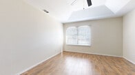 Located at 1602 S Airport Dr. in Weslaco, Texas, this single-story home offers a clean, modern aesthetic throughout. Wood-look tile flooring flows consistently across the living spaces, providing a warm yet low-maintenance finish. The spacious living area stands out with a vaulted tray ceiling and a ceiling fan, while a large window with blinds admits generous natural light and creates an open, airy atmosphere. The galley-style kitchen is well-appointed with white raised-panel cabinetry, quartz countertops featuring bold veining, a matching tile backsplash, stainless steel appliances including a range and refrigerator, and a built-in sink. Additional rooms offer ample space, each finished with the same wood-look tile flooring and fitted with ceiling fans. One bedroom features elegant arched window detailing, while another includes French doors leading outdoors and a walk-in closet with a clothing rod. The entryway features six-panel white doors, a wall-mounted thermostat, and a floor-level HVAC vent, reflecting practical, well-considered design. Neutral warm-beige walls throughout create a cohesive and inviting environment, making this home a versatile and move-in-ready space.