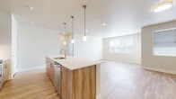 This well-appointed single-floor residence showcases a clean, modern design with a thoughtful open-concept layout. The heart of the home is a spacious kitchen and living area, where a large center island with a stainless steel sink and white quartz countertop serves as the focal point. Pendant lighting with brushed gold hardware hangs above the island, complementing warm wood-toned cabinetry and a full suite of stainless steel appliances, including a French door refrigerator, range, and built-in microwave. Light hardwood-style flooring flows throughout the main living areas, enhancing the bright, airy ambiance created by recessed lighting and natural light from large windows. The bedrooms offer plush carpeting, ceiling fans, and window blinds, providing a comfortable and quiet retreat. A dedicated walk-in closet with wire shelving adds practical storage. The bathrooms feature dual-sink vanities with wood-grain cabinetry, quartz countertops, large mirrors with vanity lighting, and hardwood-style flooring; one bathroom includes a full soaking tub and shower combination. A dedicated in-unit laundry room with a full-size washer and dryer and built-in shelving completes this functional and stylish residence.