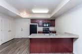 This single-floor residence is designed with an open, functional layout that seamlessly connects the kitchen and living areas. The kitchen is a standout feature, outfitted with rich dark-wood cabinetry, granite-style countertops, a central island with a double sink, and a full suite of black appliances including a gas range, microwave, dishwasher, and refrigerator. A tray ceiling with recessed lighting adds architectural interest to the kitchen space. Wood-look flooring flows throughout the main living areas, extending into a bright and airy living room equipped with a ceiling fan and large vertical-blind windows that allow generous natural light. A glass-paneled entry door provides additional light and access to the exterior. The two bedrooms are carpeted for comfort, each featuring windows with vertical blinds that bring in natural light. The primary bathroom is well-appointed with a granite-top vanity, a bathtub and shower combination, and a walk-in closet, while the secondary bathroom also features a matching granite vanity and convenient storage. Neutral warm-toned walls and consistent finishes throughout give the unit a cohesive and clean aesthetic, making it a comfortable and practical living space.