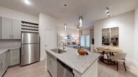 This single-floor residence features a thoughtfully designed open-concept layout connecting the kitchen, dining, and living areas. The kitchen is a standout space, equipped with gray shaker-style cabinetry, granite countertops, a large center island with bar seating and an undermount sink, stainless steel appliances including a refrigerator, electric range, and microwave, plus a subway tile backsplash and elegant pendant lighting overhead. A built-in desk nook adds functional workspace nearby.

The living area is bright and welcoming, featuring a ceiling fan, light wood-style flooring, and a glass-paned door that invites natural light. A separate dining area completes the communal space.

The unit includes multiple bedrooms, each carpeted and filled with natural light from large windows dressed with blinds and draping curtains. The primary bathroom offers a long granite-topped double vanity with white cabinetry, a frameless glass walk-in shower with tile surround, and wood-style flooring. A secondary bathroom provides a full tub-shower combination. Throughout, the color palette remains neutral and cohesive, contributing to a clean, modern ambiance.