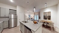 This single-floor residence features a thoughtfully designed open-concept layout connecting the kitchen, dining, and living areas. The kitchen is a standout space, equipped with gray shaker-style cabinetry, granite countertops, a large center island with bar seating and an undermount sink, stainless steel appliances including a refrigerator, electric range, and microwave, plus a subway tile backsplash and elegant pendant lighting overhead. A built-in desk nook adds functional workspace nearby.

The living area is bright and welcoming, featuring a ceiling fan, light wood-style flooring, and a glass-paned door that invites natural light. A separate dining area completes the communal space.

The unit includes multiple bedrooms, each carpeted and filled with natural light from large windows dressed with blinds and draping curtains. The primary bathroom offers a long granite-topped double vanity with white cabinetry, a frameless glass walk-in shower with tile surround, and wood-style flooring. A secondary bathroom provides a full tub-shower combination. Throughout, the color palette remains neutral and cohesive, contributing to a clean, modern ambiance.