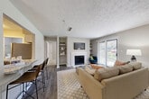This well-appointed 2-bedroom, 2-bathroom single-floor residence at 2325 Woodcrest Walk in Lithonia, GA offers a thoughtfully designed layout with modern finishes throughout. The living room serves as the heart of the home, featuring a classic white-framed fireplace flanked by built-in shelving, wood-look flooring, a textured ceiling, and a sliding glass door that opens to a private balcony with outdoor views. The adjacent kitchen is equipped with white shaker cabinetry, granite countertops, a subway tile backsplash, and stainless steel appliances, including a refrigerator, microwave, and range. A granite-topped breakfast bar connects the kitchen to the living and dining areas, offering additional seating. The dedicated dining room features a bold accent wall and pendant lighting, creating a distinct and stylish space. Both bedrooms are carpeted and fitted with ceiling fans, offering a comfortable retreat. The primary bedroom is generously sized with a dedicated closet and en-suite bathroom access. Each bathroom includes granite vanity countertops and a tub-shower combination. A utility room and additional closet space complete this functional and attractive home.