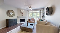 This multi-level residence spans three floors and offers a well-designed layout with a seamless blend of comfort and functionality. The main living area features rich hardwood-style flooring, a ceiling fan, and a classic fireplace framed by a white mantel. Large sliding glass doors flood the room with natural light and provide direct access to a private balcony overlooking lush greenery, creating an inviting indoor-outdoor connection.

The kitchen is a standout feature, equipped with stainless steel appliances including a range, microwave, refrigerator, and dishwasher. White cabinetry pairs cleanly with a white quartz island countertop, and warm hardwood-style flooring ties the space together. An adjacent dining area completes this open-concept entertaining zone.

The bedrooms are carpeted and well-proportioned, with windows offering treetop views that lend a serene, natural ambiance. One upper-floor bedroom benefits from vaulted ceilings and is complemented by an en-suite bathroom featuring a white vanity with modern fixtures and dual mirrors. Additional bathrooms include a full tub-shower combination with wood-look vinyl flooring.

Upper-floor hallways provide closet storage and connect the bedrooms efficiently. Throughout the home, neutral tones, recessed lighting, and clean architectural lines contribute to a cohesive and welcoming atmosphere across all three levels.