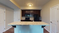 Located at 2845 Austin Manor Blvd in Columbus, Ohio, this single-floor unit offers a well-designed, open-concept layout that seamlessly connects the kitchen and living areas. The kitchen is a standout feature, outfitted with rich dark espresso cabinetry extending to the ceiling for ample storage, light granite-style countertops, and a full suite of black appliances including a range, over-the-range microwave, and refrigerator. A peninsula with a granite-topped breakfast bar provides additional counter space and a natural divide between the kitchen and the adjoining living area. The living space features a combination of durable hardwood-style flooring near the kitchen and plush carpeting extending into the main lounge area, which is brightened by a large sliding glass door fitted with vertical blinds. The bedroom is comfortably sized with soft carpeting, a window with blinds that allows natural light, and a closet with paneled doors. The bathroom is clean and functional, with tile flooring, a tub-shower combination, a toilet, and a vanity topped with a light stone-style countertop and dark cabinetry, accented by a large mirror. Neutral warm beige tones throughout the unit create a cohesive and inviting atmosphere.