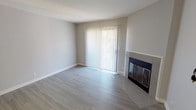 This single-floor residence offers a thoughtfully designed layout with a clean, modern aesthetic throughout. The living room serves as the heart of the space, showcasing light wood-look flooring, neutral gray walls, and a tile-surround fireplace with glass doors as a focal point. A sliding glass door fills the room with natural light and provides outdoor access. Adjacent to the living area, a ceiling fan illuminates the dining or secondary living space, which connects seamlessly to the kitchen through a convenient pass-through window. The galley-style kitchen is well-appointed with white shaker cabinets, granite-look countertops, stainless steel appliances including a refrigerator, range, microwave, and dishwasher, and a skylight that brightens the workspace. The bedroom features plush carpeting, soft neutral tones, and a window with vertical blinds offering natural light and privacy. The bathroom is finished with granite-look countertops, a full tub-shower combination with curved rod, and wood-look tile flooring. A dedicated laundry area houses a full-size side-by-side washer and dryer. The overall ambiance is bright, clean, and move-in ready.