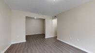 This single-floor residence offers a clean, modern aesthetic with consistent wood-look flooring flowing throughout the living areas and bedrooms. The open layout is anchored by a bright living room featuring a sliding glass door dressed with vertical blinds, allowing natural light to fill the space and providing access to the outdoors. Neutral beige walls and crisp white baseboards create a cohesive, move-in-ready environment across every room.

The kitchen is efficiently designed in a galley configuration, outfitted with white cabinetry, granite-style countertops, a full suite of white appliances including a refrigerator, dishwasher, and range, and a separate door for added convenience.

The bedrooms are generously proportioned, with one featuring a walk-in closet equipped with wire shelving, providing ample storage. Additional rooms include recessed alcove spaces suitable for dining or flexible use.

The bathroom is a standout feature, finished with large-format marble-look tile on both the floor and full tub surround, complemented by a white vanity — lending a polished, spa-like quality to the space.

Central HVAC vents are present throughout, ensuring year-round comfort. The overall design emphasizes simplicity and functionality, making this a well-balanced and practical living space.