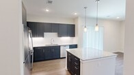 This thoughtfully designed one-bedroom, one-bathroom residence at 2300–2380 Mayall Trail offers a efficient and modern living experience across a single floor. The kitchen serves as the centerpiece of the home, showcasing bold dark navy shaker-style cabinetry, light granite countertops, and a full suite of stainless steel appliances including a refrigerator, range, microwave, and dishwasher. A central island with pendant lighting adds both workspace and visual appeal, while light hardwood-style flooring and recessed lighting throughout create a bright, cohesive atmosphere. A dedicated closet off the kitchen provides convenient built-in shelving for additional storage. The open layout connects the kitchen seamlessly to the living area, which features a ceiling fan and a window that allows natural light to fill the space. The bedroom is generously sized with plush carpeting, a large window with views of the surrounding neighborhood, and ample room for furnishings. The bathroom is clean and functional, featuring a walk-in glass-enclosed shower, granite-topped vanity, and direct access to a dedicated closet. Throughout the home, neutral wall tones, clean white trim, and consistent finishes contribute to a modern, move-in-ready aesthetic.