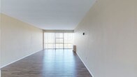 Located at 16000 Terrace Rd in East Cleveland, Ohio, this single-floor unit offers a clean, functional layout with a variety of finishes throughout. The spacious living area is a standout feature, boasting durable hardwood-style flooring and expansive floor-to-ceiling sliding glass doors dressed with vertical blinds, allowing an abundance of natural light and offering open outdoor views. The layout connects seamlessly to additional rooms via a central hallway. The kitchen is well-equipped with white cabinetry, a tile backsplash, ample counter space, and includes a refrigerator, electric range, dishwasher, and a sink — all finished with hardwood-style flooring that continues the cohesive aesthetic. The bedrooms are carpeted for comfort, with one room featuring a generous reach-in closet with a rod for hanging storage and access to an additional adjoining room. A second bedroom includes a ceiling fan with light fixture. The bathroom is appointed with classic white tile walls, a tub-shower combination with sliding glass doors, a vanity with a mirrored medicine cabinet, and chrome fixtures. Throughout, the neutral warm-toned walls and clean lines create a bright, move-in-ready atmosphere.