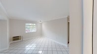 Located in the desirable Pinecrest neighborhood of South Florida, this single-story home offers a clean, functional layout with a neutral design palette throughout. The living areas are finished with gleaming white ceramic tile flooring set on the diagonal, complemented by crown molding and soft white walls that maximize the sense of light and space. Windows dressed with horizontal blinds bring in natural light while maintaining privacy, and the rooms connect seamlessly, offering an open and airy flow.

The kitchen is well-appointed with warm wood cabinetry, dark granite-style countertops, a bold dark tile backsplash, and stainless steel appliances including a built-in microwave and range. White tile flooring continues through this space, maintaining a cohesive look. A window above the counter area allows for natural light to brighten the workspace.

The bedrooms feature rich wood-tone laminate flooring and are equipped with wall-mounted air conditioning units and track lighting, offering both comfort and practicality. Large windows frame lush greenery outside, bringing a sense of the surrounding South Florida landscape into the rooms.

The bathroom is neatly finished with a dark-framed vanity mirror, a vessel-style sink set in a dark countertop, and a clean white tub-shower combination, all tied together with tile flooring for a crisp, updated look.