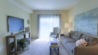 Located at 785 Cross Pointe Road in Gahanna, Ohio, this single-floor residence offers a comfortable and well-appointed living environment. The living room serves as the heart of the space, characterized by soft, neutral-toned walls that create a calm and inviting atmosphere. Plush wall-to-wall carpeting adds warmth underfoot, while a large sliding glass door fitted with vertical blinds floods the room with abundant natural light and provides a view to the outdoors. The living area is generously sized, comfortably accommodating a full sofa, accent chair, and coffee table arrangement, making it well-suited for both relaxing and entertaining. A flat-screen TV mounted on a console table anchors one side of the room, balanced by tasteful decorative accents including wall art and greenery. A floor lamp in the corner adds additional ambient lighting options. The overall design aesthetic is clean and approachable, with a light color palette throughout that enhances the sense of openness. The single-level layout offers ease of accessibility and a cohesive flow throughout the home, making this Gahanna property a practical and pleasant place to live.