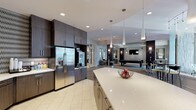 Located at 4451 Vilana Rd in Raleigh, NC, this single-floor community clubhouse is designed with a contemporary aesthetic and offers a wide array of amenity spaces for socializing, working, and relaxing. The main gathering area serves as the heart of the facility, featuring a billiards table, wall-mounted television, high-top bar tables with woven stools, and dark accent columns that lend a sleek, upscale atmosphere. Pendant lighting and wall sconces add warmth throughout the open layout.

The fully equipped kitchen is a standout feature, boasting a large quartz island with pendant lighting overhead, dark wood cabinetry, stainless steel appliances including a French door refrigerator, and a bold patterned tile backsplash. An adjacent lounge area provides comfortable seating with plush sofas in neutral tones, ideal for casual gatherings.

A dedicated business center offers built-in workstations with computers and overhead storage cabinets, complemented by a comfortable seating area and framed artwork. A separate meeting nook features a round table with yellow accent chairs, hardwood-style flooring, and large windows that bring in natural light and exterior views. Welcoming corridor seating areas with accent chairs and curated artwork complete this thoughtfully designed community space.