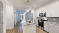 Located at 2606 Fessey Park Rd in Berry Hill, Tennessee, this well-appointed one-bedroom, one-bathroom residence offers a thoughtfully designed single-floor layout. The open-concept kitchen serves as the heart of the home, showcasing crisp white cabinetry, a subway tile backsplash, and a large granite-topped island with an undermount sink and stylish globe pendant lighting overhead. Stainless steel appliances, including a range, microwave, and refrigerator, complete the modern kitchen setup. Hardwood-style flooring runs throughout the main living areas, adding warmth and continuity to the space. The living area features French doors with transom windows above, allowing natural light to fill the room. The bedroom is carpeted for comfort and includes a ceiling fan and a window with blinds. The bathroom is accessed directly from the bedroom and features a glass-enclosed walk-in shower and hardwood-style flooring. A dedicated walk-in closet off the bathroom provides generous storage with multi-level wire shelving. Stylish gray interior doors with raised panel detailing add a consistent, contemporary aesthetic throughout, making this a polished and functional residence.
