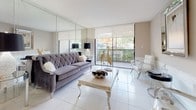 This well-appointed single-floor residence combines contemporary design with functional living spaces throughout. The kitchen is outfitted with granite countertops, crisp white cabinetry, and stainless steel appliances, including a French door refrigerator and built-in microwave, all set atop gleaming large-format tile flooring that extends throughout the home.

The living room is a bright, open space featuring floor-to-ceiling mirrored wall panels that amplify natural light and create a sense of expansiveness. Sliding glass doors lead to a private balcony, offering views of mature tropical landscaping. The adjacent dining area continues the elegant aesthetic with a mirrored accent wall, a decorative pendant light fixture, and polished tile flooring.

The primary bedroom features a calming blue accent wall, natural light from a large window with outdoor views, and tile flooring. A secondary bedroom is similarly bright and comfortable, with a window framing lush greenery. A spacious walk-in closet with white wire shelving and hanging rods provides generous storage. The bathroom features granite countertops, a white vanity, and clean tile throughout.

Elegant wainscoting detail in one area of the home adds a refined architectural touch, rounding out this thoughtfully designed and move-in ready residence.