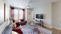 This single-floor unit at Campus Circle offers a well-organized layout across four bedrooms and four bathrooms, making it well-suited for shared living. The kitchen is a standout feature, showcasing dark espresso cabinetry, granite-style countertops, stainless steel appliances including a refrigerator, microwave, and electric range, and a multi-seat breakfast bar with pendant lighting overhead. Wood-style flooring runs through the kitchen and living areas, adding warmth and visual continuity throughout the common spaces.

The living room receives generous natural light through large windows dressed with floor-length curtains, and is equipped with a ceiling fan. Each of the four bedrooms features carpeted flooring, a window with exterior views, and a private en-suite bathroom. The bathrooms maintain a consistent design with dark wood vanities, granite-topped sinks, large mirrors, and shower-tub combinations. Individual bedrooms also feature private entry doors, providing added privacy for each occupant. A central hallway connects the bedrooms and common areas, contributing to a functional and efficient floor plan throughout.