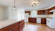 Located at 1335B Mertensia Rd in Farmington, NY, this three-bedroom, two-bathroom home spans three floors, offering a well-organized layout with ample living space. The main level features a combined kitchen and dining area, where rich, dark-stained wood cabinetry lines the walls alongside light granite-style countertops. White appliances, including a refrigerator, dishwasher, and range, complement the space, while light hardwood-style flooring and a decorative flush-mount light fixture add warmth. A kitchen island provides additional prep and storage space. The entry foyer greets visitors with an arched-window front door and a large closet for convenient storage. The living areas continue with neutral wall tones and consistent hardwood-style flooring throughout. Three bedrooms offer comfortable proportions, with windows framing views of the surrounding greenery and neighborhood. The bathrooms are cleanly finished with hardwood-style flooring, a tub/shower combination, and a window providing natural light. The unfinished basement presents a generous open footprint with a concrete floor, exposed wood-beam ceiling, and small windows — ideal for storage or future use. A balcony and five closets round out this practical, move-in-ready home.
