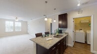 This single-floor residence offers a thoughtfully designed open-concept layout that seamlessly connects the kitchen and living areas. The kitchen is a standout feature, showcasing rich dark cabinetry, granite countertops, and a peninsula with bar seating illuminated by pendant lighting. Stainless steel appliances—including a refrigerator, range, and microwave—complement the wood-look flooring that flows throughout the kitchen and dining space. Crown molding adds a refined touch throughout the common areas.

The spacious living room is finished with plush carpeting, a ceiling fan, and multiple windows that invite abundant natural light. An open entryway connects the kitchen to this generous gathering space. The bedrooms are carpeted and well-sized, with one featuring a walk-in closet equipped with built-in shelving. Windows in the bedrooms offer views to the outside, enhancing the sense of openness.

The bathroom is finished with dark cabinetry, a granite-topped vanity, a large mirror with lighted fixture, wood-look flooring, and a tiled shower-tub combination. The overall palette of neutral tones, consistent finishes, and cohesive design elements creates a clean, comfortable, and functional living environment throughout the space.