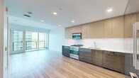This well-appointed two-floor residence offers a thoughtfully designed layout spread across a compact yet efficiently utilized footprint. The lower level houses an open-plan kitchen and living area, while the upper level accommodates the bedroom, bathroom, and closet.

The kitchen is a standout feature, outfitted with high-gloss dark cabinetry contrasted by warm taupe upper cabinets and a marble-style tile backsplash. Stainless steel appliances, including a gas range with microwave overhead and a full-size French door refrigerator, complete the contemporary look. Light hardwood flooring flows throughout, enhancing the clean, modern aesthetic.

The living area benefits from expansive floor-to-ceiling sliding glass doors that open onto a glass-railed balcony, offering sweeping views of the surrounding cityscape and parkland beyond. Abundant natural light fills the space throughout the day.

The bedroom features its own balcony access via a glass sliding door, framing urban views and continuing the bright, airy feel of the home. The bathroom is finished in a clean, minimalist style with a floating wood-toned vanity, backlit mirror, and a glass-enclosed walk-in shower, completing the modern design language present throughout this residence.