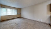 Located at 930-940 N Murray Blvd in Colorado Springs, CO, this one-bedroom, one-bathroom unit offers a practical and efficient single-floor layout. The space is organized around a central hallway finished with wood-look flooring that connects the main areas. The living room is carpeted and spacious enough for comfortable furnishings, featuring a wall-mounted air conditioning unit, a baseboard heater, and a large window with vertical blinds that allows natural light to fill the room. The kitchen is galley-style, equipped with warm oak cabinetry, a tile mosaic backsplash, laminate countertops, a double-basin sink, and white appliances including a refrigerator and range. The bedroom, also carpeted, provides a comfortable retreat with a sliding-door closet offering ample storage, a baseboard heater, and a window for natural light. A second closet is accessible from the hallway, adding extra storage capacity. The bathroom features a wood-framed vanity with a mirrored medicine cabinet above the sink and wood-look flooring. Throughout the unit, textured ceilings and neutral warm-beige walls create a cohesive, understated aesthetic suited for everyday living.