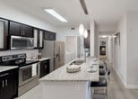 Located at 20941 San Simeon Way in Miami, FL, this well-appointed single-floor residence offers a contemporary design throughout. The open-concept kitchen is a standout feature, boasting granite countertops, dark espresso cabinetry, stainless steel appliances, and a large center island with bar seating, illuminated by elegant pendant lighting. A dedicated dining area sits adjacent to the kitchen, creating a seamless flow for entertaining. In-unit laundry is conveniently accessible from the kitchen corridor.

The living area is bright and welcoming, featuring light tile flooring, a ceiling fan, and floor-to-ceiling sliding glass doors that open to a private outdoor patio with views of lush greenery. The bedrooms are carpeted for comfort; the primary bedroom includes a spacious closet and ample natural light, while additional bedrooms offer generous closet space and large windows.

Two well-designed bathrooms serve the residence. The primary bath features a glass-enclosed walk-in shower, granite vanity, and dark-framed mirror, while the secondary bath includes a tub-shower combination and matching granite finishes. Light tile flooring runs throughout the wet areas, tying the aesthetic together. The overall design palette of crisp whites, dark accents, and granite surfaces lends the space a clean, modern ambiance.