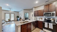 This thoughtfully designed single-floor residence offers a cohesive blend of modern finishes and comfortable living spaces throughout. The open-concept kitchen serves as a central hub, showcasing rich dark-wood cabinetry, granite countertops, a subway tile backsplash, stainless steel appliances, and a peninsula island with bar seating — ideal for casual dining or entertaining. Wood-look flooring flows through the main living areas, adding warmth and continuity. The living room is bright and welcoming, featuring crown molding, a ceiling fan, and double doors that invite natural light from outside. The primary bedroom is generously proportioned, with plush carpeting, dual windows, and a ceiling fan, while the en-suite bathroom features a granite-topped double vanity with rich cabinetry and a walk-in shower. A second bedroom offers the same comfortable carpeted finish and ample natural light. A versatile additional room functions as a dedicated home office, complete with carpeting, a ceiling fan, and a window with drape treatments. The secondary bathroom includes a full soaking tub and shower combination with built-in shelving. Completing the layout is a convenient in-unit laundry area, adding everyday practicality to this well-rounded residence.