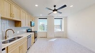 Located at 101 N Broadway Ave in the heart of downtown Oklahoma City, this studio unit offers an efficient, well-designed single-floor layout. The open-concept main area seamlessly combines the living room, dining space, and kitchen, creating a versatile and functional environment. Large windows flood the space with abundant natural light while framing views of the surrounding urban skyline. A ceiling fan with integrated lighting serves as a central fixture, enhancing airflow and ambiance throughout the main area.

The kitchen is outfitted with light wood cabinetry accented by gold hardware, a neutral tile backsplash, white countertops, and a full suite of stainless steel appliances including a refrigerator, range, microwave, and dishwasher. Light-toned carpeting runs throughout the living area, contributing to the clean, bright aesthetic.

A hallway connects the main living area to the remaining rooms, including a closet and a dedicated laundry space. The bathroom is a standout feature, showcasing floor-to-ceiling marble-look tile surrounding the tub-shower combination, complemented by brushed gold fixtures, classic hex mosaic tile flooring, and light wood cabinetry. The overall design palette is crisp and modern, making this an efficient urban unit well-suited for downtown living.