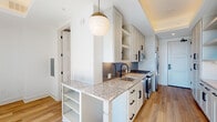 Located at 1301 Spring St NW in Atlanta's vibrant Midtown neighborhood, this contemporary single-floor unit offers a thoughtfully designed layout with high-end finishes throughout. The galley-style kitchen is a standout feature, showcasing crisp white shaker cabinetry with matte black hardware, granite countertops, a stainless steel undermount sink with a black faucet, and a full suite of stainless steel appliances including a gas range, microwave, and refrigerator. Open shelving and a tray ceiling with warm accent lighting add both function and elegance to the space. Light hardwood flooring runs throughout, creating a warm, cohesive aesthetic. The living area is anchored by dramatic floor-to-ceiling windows and a sliding glass door that frame sweeping panoramic views of the Atlanta skyline and cityscape, flooding the interior with abundant natural light. The bathroom is finished with a striking combination of bold cobalt blue and white vertical tile surrounding a soaking tub, complemented by granite vanity countertops and neutral floor tile. Together, the modern design elements, quality materials, and elevated city views make this a refined and visually compelling urban residence.