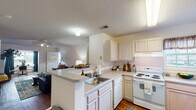 This single-story residence offers a functional and comfortable layout designed for everyday living. The open-concept kitchen flows seamlessly into the living area, featuring light wood cabinetry, a full suite of white appliances including an electric range, dishwasher, and refrigerator, plus a peninsula with bar seating that serves as both a prep space and casual dining spot. A window above the sink brings in natural light, while the textured ceiling adds a classic architectural detail.

The living room is a welcoming central gathering space, outfitted with a ceiling fan and light fixture, and flanked on either side by access to the bedrooms—creating a convenient and connected layout. Rich hardwood-style flooring runs throughout the common areas and bedrooms, adding warmth and cohesion to the space.

Each bedroom is generously sized, accommodating a full bed and desk area with ease. One bedroom features a window with blinds offering natural light, while another benefits from an en-suite bathroom access. Both bathrooms are well-equipped with walk-in showers or tub-shower combos, over-toilet cabinetry for storage, vanity mirrors, and hardwood-style flooring. The entryway provides a welcoming transition into the home with ample space and direct access to the main living areas.