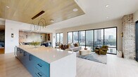 Located in Atlanta's dynamic West Midtown neighborhood, this thoughtfully designed amenity lounge offers an open, single-floor layout that seamlessly blends social, dining, and meeting functions. Floor-to-ceiling black-framed windows dominate the main living area, flooding the space with natural light and framing sweeping panoramic views of the Atlanta skyline. Light hardwood-style flooring runs throughout, complementing the bright, airy palette.

The wet bar and kitchen area is a standout feature, showcasing teal-blue cabinetry with matte black hardware, a quartz waterfall island with seating, a wine refrigerator, open wood shelving, and a decorative scallop-patterned tile backsplash. Dramatic arched pendant lights with brass accents hang overhead beneath a warm wood-paneled ceiling.

The lounge area provides generous seating with plush sofas, accent chairs, and an intimate banquette nook with a textured metallic accent wall. A private conference room features a round oak table, velvet blue chairs, a tray ceiling with a sculptural gold chandelier, and direct access to an outdoor terrace.

Exposed brick columns frame the terrace entry, adding a warm industrial character that contrasts beautifully with the space's modern finishes, making this lounge a versatile and visually compelling gathering destination.