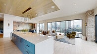 Located in Atlanta's dynamic West Midtown neighborhood, this thoughtfully designed amenity lounge offers an open, single-floor layout that seamlessly blends social, dining, and meeting functions. Floor-to-ceiling black-framed windows dominate the main living area, flooding the space with natural light and framing sweeping panoramic views of the Atlanta skyline. Light hardwood-style flooring runs throughout, complementing the bright, airy palette.

The wet bar and kitchen area is a standout feature, showcasing teal-blue cabinetry with matte black hardware, a quartz waterfall island with seating, a wine refrigerator, open wood shelving, and a decorative scallop-patterned tile backsplash. Dramatic arched pendant lights with brass accents hang overhead beneath a warm wood-paneled ceiling.

The lounge area provides generous seating with plush sofas, accent chairs, and an intimate banquette nook with a textured metallic accent wall. A private conference room features a round oak table, velvet blue chairs, a tray ceiling with a sculptural gold chandelier, and direct access to an outdoor terrace.

Exposed brick columns frame the terrace entry, adding a warm industrial character that contrasts beautifully with the space's modern finishes, making this lounge a versatile and visually compelling gathering destination.
