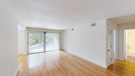 Located at 2700 Brigadoon Drive in Raleigh, NC, this single-floor, 2-bedroom, 1-bathroom home offers a clean, well-designed layout with consistent hardwood flooring throughout. The living area is bright and open, highlighted by a sliding glass door flanked by vertical blinds that opens to a private balcony with outdoor views, allowing generous natural light to fill the space. A ceiling fan adds comfort to the adjoining area, which also features a large window overlooking the greenery outside. The galley-style kitchen is efficiently arranged with white cabinetry, dark countertops, and white appliances including an electric range and refrigerator, with light wood-tone flooring completing the look. Both bedrooms are well-proportioned and bathed in natural light. The primary bedroom is notably spacious and features a sliding closet with vertical shiplap-style paneling, a large window, and polished hardwood floors. The second bedroom offers similar finishes with a charming accent wall of vertical white paneling. The full bathroom includes a tub-shower combination, toilet, and vanity. A hallway connects the rooms, and the overall palette of crisp white walls and warm wood floors gives the home a bright, clean, and welcoming ambiance throughout.