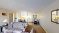 Located at 501-567 Canyon in Oceanside, this single-story model unit presents a well-organized layout designed for comfortable everyday living. The open-concept living and dining area forms the heart of the home, featuring neutral-toned carpet, textured ceilings, and warm beige walls that create a cohesive, inviting atmosphere throughout. A pass-through counter with bar seating connects the living space to the kitchen, enhancing the sense of openness and making the area well-suited for casual dining and entertaining.

The kitchen is efficiently arranged with ample white cabinetry providing generous storage, white appliances including a refrigerator, range, and dishwasher, a stainless steel sink, and light stone-style tile flooring. The clean, bright aesthetic makes the space practical and easy to navigate.

The bedroom is a comfortable, carpeted retreat featuring a large window dressed with vertical blinds that allows natural light to filter in while offering views of the surrounding area. The room offers direct access to the bathroom, which is finished with a full tub and shower combination and clean white fixtures. A closet provides additional storage within the bedroom.

Overall, the unit maintains a consistent neutral palette and functional design throughout, offering a straightforward and livable single-floor residence.