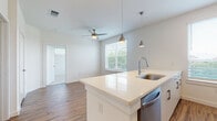 This single-floor residence offers a thoughtfully designed open-concept layout with clean, modern finishes throughout. The kitchen serves as a central highlight, featuring crisp white cabinetry, a large quartz island with an undermount stainless steel sink, and a full suite of stainless steel appliances including a range, microwave, refrigerator, and dishwasher. Stylish pendant lighting hangs above the island, complementing the bright, airy atmosphere created by multiple windows dressed with horizontal blinds. Warm wood-look flooring flows through the kitchen and living areas, adding a natural contrast to the white palette. The living area extends naturally from the kitchen and includes a ceiling fan, making it a comfortable and functional shared space. The bedroom is carpeted for added comfort and benefits from a large window that invites ample natural light and outdoor views. The bathroom is finished to a high standard, featuring a wide quartz vanity with white cabinetry, a large frameless mirror, and a full tub and shower surround clad in dramatic marble-look tile with bold veining. Recessed lighting and wood-look flooring complete the bathroom's refined aesthetic. Overall, this residence combines modern design with practical functionality.