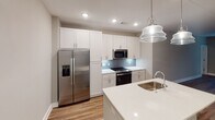 Located at 6131 Ruisseau St in Charlotte, NC, this single-floor home offers a well-designed layout with contemporary finishes throughout. The open-concept living and dining area features rich hardwood-style flooring, neutral gray walls, and large windows fitted with blinds that invite natural light while maintaining privacy. A glass-panel door provides direct access to the outdoors, enhancing the connection between interior and exterior spaces.

The kitchen is a standout feature, equipped with white shaker-style cabinetry extending to the ceiling for generous storage, a herringbone-patterned blue tile backsplash, and bright white quartz countertops. A central island with a stainless steel sink and pendant lighting anchors the space, complemented by a full suite of stainless steel appliances including a refrigerator with ice maker, electric range, and built-in microwave.

The bedrooms are carpeted for comfort, each offering multiple windows and ceiling fans for climate control. The bathrooms are well-appointed with double-sink vanities topped in white quartz, large mirrors with chrome sconce lighting, white cabinetry, and hardwood-style flooring. The primary bath includes a tub-shower combination with clean tile surround. Throughout the home, crisp white trim and doors provide a polished, cohesive aesthetic.