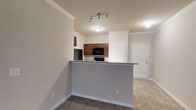 This single-floor, 3-bedroom, 2-bathroom residence offers a well-designed layout that maximizes both comfort and functionality. The open-concept living and kitchen area serves as the heart of the home, creating a seamless flow between spaces ideal for everyday living and entertaining. The kitchen features warm medium-toned wood cabinetry, dark granite or stone-look countertops, and black appliances including a refrigerator, range, and over-the-range microwave. A raised breakfast bar peninsula separates the kitchen from the living area, providing additional seating and prep space. Track lighting above the kitchen ensures bright, directed illumination, complementing the recessed and flush-mount ceiling fixtures throughout. Crown molding adds a refined architectural touch along the ceiling lines, enhancing the overall aesthetic. The flooring transitions between plush carpet in the living areas and tile in the kitchen and entryway zones, offering both comfort and practicality. Neutral wall tones throughout create a clean, versatile backdrop. A paneled entry door provides a welcoming focal point, rounding out a thoughtfully appointed home designed for comfortable, move-in-ready living.