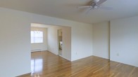 This single-floor residence offers a clean, open layout filled with natural light and classic design elements. The main living area features gleaming hardwood floors that reflect light beautifully throughout the space, contributing to a bright and airy ambiance. A ceiling fan overhead provides year-round comfort and adds a practical touch to the room.

The living area flows seamlessly into a dedicated dining space, defined by an elegant chandelier that adds a touch of refinement. A large window in the dining area invites abundant natural light, enhancing the sense of openness. A baseboard heating system runs along the wall, ensuring warmth during cooler months.

Adjacent to the dining area, the kitchen is visible through an open passageway, featuring tiled walls, white appliances, and cabinetry that provide a functional and tidy cooking environment. The neutral, cream-toned walls throughout the space create a versatile backdrop, making it easy to personalize with furnishings and décor.

Overall, this residence presents a well-connected, single-level floor plan that balances practicality with comfort. The polished hardwood floors, natural lighting, and cohesive neutral palette come together to create a warm, inviting atmosphere suited to a variety of lifestyles.