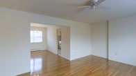 This single-floor residence offers a clean, open layout filled with natural light and classic design elements. The main living area features gleaming hardwood floors that reflect light beautifully throughout the space, contributing to a bright and airy ambiance. A ceiling fan overhead provides year-round comfort and adds a practical touch to the room.

The living area flows seamlessly into a dedicated dining space, defined by an elegant chandelier that adds a touch of refinement. A large window in the dining area invites abundant natural light, enhancing the sense of openness. A baseboard heating system runs along the wall, ensuring warmth during cooler months.

Adjacent to the dining area, the kitchen is visible through an open passageway, featuring tiled walls, white appliances, and cabinetry that provide a functional and tidy cooking environment. The neutral, cream-toned walls throughout the space create a versatile backdrop, making it easy to personalize with furnishings and décor.

Overall, this residence presents a well-connected, single-level floor plan that balances practicality with comfort. The polished hardwood floors, natural lighting, and cohesive neutral palette come together to create a warm, inviting atmosphere suited to a variety of lifestyles.