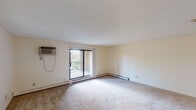 Located at 14625 Portland Ave in Burnsville, MN, this single-floor residential unit offers a well-organized layout designed for comfortable everyday living. The generously sized living area features neutral-toned carpet, a textured ceiling, and a wall-mounted air conditioning unit. A large sliding glass door opens to a private balcony, bringing in natural light and offering pleasant outdoor views of surrounding greenery. The transition from the living area to adjacent spaces is marked by a shift from hardwood-style flooring to carpet, creating distinct zones within the open layout. The kitchen is outfitted with bold dark cabinetry contrasted against light countertops, a double stainless steel sink, and a black electric range, providing a functional and visually striking cooking space. The bedrooms are carpeted and bright, each featuring closets and baseboard heating, with windows dressed in vertical blinds that diffuse natural light. Two bathrooms serve the unit — one featuring a soaking tub, a large mirror, and vanity lighting, while the second includes hardwood-style flooring, a wall-mounted towel bar, and a streamlined vanity. Baseboard heating is present throughout, ensuring consistent warmth. The overall aesthetic is clean and neutral, offering a versatile canvas well-suited to a variety of interior styles.