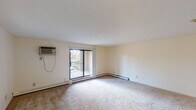 Located at 14625 Portland Ave in Burnsville, MN, this single-floor residential unit offers a well-organized layout designed for comfortable everyday living. The generously sized living area features neutral-toned carpet, a textured ceiling, and a wall-mounted air conditioning unit. A large sliding glass door opens to a private balcony, bringing in natural light and offering pleasant outdoor views of surrounding greenery. The transition from the living area to adjacent spaces is marked by a shift from hardwood-style flooring to carpet, creating distinct zones within the open layout. The kitchen is outfitted with bold dark cabinetry contrasted against light countertops, a double stainless steel sink, and a black electric range, providing a functional and visually striking cooking space. The bedrooms are carpeted and bright, each featuring closets and baseboard heating, with windows dressed in vertical blinds that diffuse natural light. Two bathrooms serve the unit — one featuring a soaking tub, a large mirror, and vanity lighting, while the second includes hardwood-style flooring, a wall-mounted towel bar, and a streamlined vanity. Baseboard heating is present throughout, ensuring consistent warmth. The overall aesthetic is clean and neutral, offering a versatile canvas well-suited to a variety of interior styles.