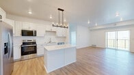 Located on 62nd Ave S in Fargo, North Dakota, this well-appointed residence offers four bedrooms and three bathrooms across a thoughtfully designed single-floor layout. The open-concept living area features light-toned hardwood-style flooring and recessed lighting, culminating in a sliding glass door that opens to a private balcony with outdoor views — filling the space with natural light.

The kitchen is a standout feature, showcasing crisp white shaker cabinetry with matte black hardware, light quartz countertops, a central island, and a full suite of stainless steel appliances including a French door refrigerator, range, microwave, and dishwasher. Warm hardwood-style flooring runs throughout the main living and kitchen areas.

The bedrooms are carpeted for comfort, with clean white walls and natural light provided by windows with blinds. The primary bedroom includes a walk-in closet with wire shelving. The bathrooms are finished with white vanities, quartz countertops, matte black fixtures, and hardwood-style flooring. One bathroom features a full tub-shower combination. Throughout the space, a consistent modern aesthetic is maintained with a neutral white palette, creating a clean and functional living environment.
