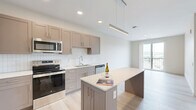 Located at 501 W Washington St in East Peoria, IL, this well-designed one-bedroom, one-bathroom unit offers a thoughtful layout across a single floor. The open-concept kitchen and living area serves as the heart of the space, showcasing taupe shaker-style cabinetry, white subway tile backsplash, a large kitchen island with a light quartz countertop, and a full suite of stainless steel appliances including a refrigerator, range, microwave, and dishwasher. Light wood-look flooring runs throughout the main living areas, contributing to a clean, contemporary aesthetic. The living area features a sliding glass door that opens to a private balcony, offering open outdoor views and an abundance of natural light. The bedroom is a comfortable retreat, carpeted for warmth, and features a ceiling fan and a wide window that frames scenic views. A dedicated walk-in closet with wire shelving provides generous storage. The bathroom is finished with light tile flooring, a single-sink vanity with a dark wood cabinet, a framed mirror, and a full soaking tub with shower. Neutral tones and modern finishes are carried consistently throughout, giving the unit a cohesive and move-in-ready feel.