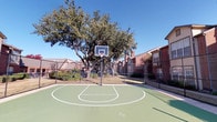 This community amenity space centers on a well-maintained outdoor basketball court, offering a spacious playing surface finished in a smooth green coating with clearly marked regulation lines, including a painted key and three-point arc. A sturdy, fixed basketball hoop with a standard backboard stands at one end of the court, providing a complete playing experience. The court is fully enclosed by chain-link fencing, ensuring safety and defining the play area. A large, mature tree positioned beyond the court's perimeter provides natural shade and a pleasant visual backdrop, while the surrounding brick residential buildings frame the space and contribute to a sense of community. The open-air setting benefits from abundant natural light beneath clear skies, creating an inviting outdoor environment for recreation.

The interior kitchen is compact yet efficiently designed, featuring rich dark cabinetry with ample upper and lower storage. Granite countertops with warm, variegated tones provide a durable and attractive work surface. A mosaic tile backsplash in blue, brown, and neutral tones adds a decorative element throughout. Black appliances, including a range, over-the-range microwave, and refrigerator, complement the cabinetry and contribute to a cohesive, contemporary aesthetic.