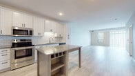 This single-floor residence offers a clean, contemporary aesthetic with thoughtfully designed living spaces and quality finishes throughout. The open-concept kitchen is a standout feature, showcasing crisp white shaker-style cabinetry, a classic subway tile backsplash, stainless steel appliances including a French door refrigerator, electric range, and built-in microwave, and a granite-topped island with integrated wine storage and open shelving below. Light wood-look flooring runs seamlessly through the kitchen and into the expansive living area, enhancing the bright and airy feel. Large windows allow natural light to fill the generous living space, which offers a clean, neutral palette ideal for a variety of furnishing styles. The bedrooms provide a comfortable contrast with plush wall-to-wall carpeting, closet access, and natural light from well-placed windows. The bathroom is finished with matching granite countertops, white cabinetry with matte black hardware, and a full tub-shower combination. Consistent design elements — including panel-style interior doors with matte black hardware and neutral wall tones — create a cohesive and modern feel throughout the entire space.