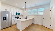 Located at 4418 Oat Grass Circle in Charlotte, NC, this modern four-story home offers 3 bedrooms, 4 bathrooms, and a thoughtfully designed layout across each level. The ground floor features an attached garage with an automatic opener, providing convenient and secure parking. The main living level showcases a bright, open-concept space that seamlessly combines the kitchen, dining, and living areas. The kitchen is outfitted with white shaker cabinetry, a white quartz peninsula with a undermount sink and matte black fixtures, stainless steel appliances, and pendant lighting — all set atop warm light hardwood flooring that flows throughout the home. A clean, light-filled hallway with wood-tread staircase connects the floors. The upper levels house three well-proportioned bedrooms, each featuring natural light from large windows with views of the surrounding neighborhood. The primary bedroom includes a ceiling fan and a walk-in closet with wire shelving. Additional closets are distributed across the home — six in total — offering generous storage. The bathrooms feature white vanities with quartz counters and matte black hardware. A dedicated laundry room and a versatile loft on the top floor round out this well-appointed home, ideal for flexible living in Charlotte.