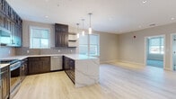 Located at 50 Main St in Hackensack, NJ, this thoughtfully designed single-floor residence combines modern finishes with functional living spaces. The heart of the home is a stunning open-concept kitchen, anchored by a large center island with a striking marble-look quartz countertop and pendant lighting overhead. Rich, dark-toned cabinetry extends floor to ceiling, providing generous storage, while stainless steel appliances — including a gas range, built-in microwave, dishwasher, and refrigerator — lend a professional quality to the space. A herringbone-patterned tile backsplash adds a refined decorative touch. Light hardwood flooring flows throughout the main living areas, enhancing the bright and airy atmosphere created by recessed lighting and large windows. The bedrooms are comfortably appointed with plush carpeting, ceiling fans, and large windows that frame views of the surrounding Hackensack cityscape. The bathroom features a dark wood vanity with ample storage, a tiled tub-shower combination with brushed nickel fixtures, and light tile walls that create a clean, cohesive aesthetic. Additional rooms with hardwood floors offer flexible use as a home office or den. This well-finished residence delivers a polished urban living experience in the heart of downtown Hackensack.