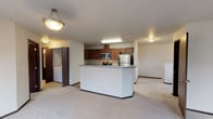 Located at 15001 North Wandermere Road in Spokane, Washington, this single-floor unit offers a functional and well-appointed layout designed for comfortable living. The open-concept design connects the kitchen and living areas seamlessly, creating a spacious and versatile environment.

The kitchen is a standout feature, equipped with rich dark wood cabinetry, light-toned countertops, and a full suite of stainless steel appliances including a refrigerator, range, and over-the-range microwave. A central island with additional counter space enhances both storage and meal preparation. Light wood-look flooring grounds the kitchen area, providing a clean contrast to the warm cabinetry.

The living area is generously sized, featuring plush neutral carpeting and large windows that invite abundant natural light. Sliding glass doors open to an outdoor balcony, offering views of the surrounding neighborhood. The bedrooms are well-proportioned, each finished with soft carpeting and windows providing exterior views.

The bathrooms are neatly appointed with dark wood vanities, light countertops, tile-style flooring, and a full tub and shower combination. Throughout the unit, dark baseboards provide a consistent design accent against the neutral walls. The overall ambiance is clean, practical, and move-in ready, suited for everyday living in north Spokane.