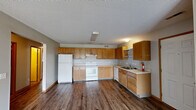 Located at 802 Dickinson Ave in Ames, Iowa, this single-floor, three-bedroom, two-bathroom home offers a practical and well-organized layout. The open-concept kitchen and living area serves as the heart of the home, featuring warm oak cabinetry with ample upper and lower storage, light countertops, and white appliances including a range, refrigerator, and dishwasher. Rich, dark hardwood-style flooring runs throughout the main living areas, complementing the neutral gray walls and wood-toned trim. The living room is spacious and bright, equipped with a ceiling fan and vertical blind-covered sliding doors that invite natural light. A central hallway connects the bedrooms, each finished with plush carpet and generous closet space — with five closets total throughout the home. The primary bedroom offers comfortable proportions and its own closet access. Both bathrooms are finished with oak vanities, white countertops, and large mirrors. A dedicated utility room adds practical storage and functionality. Textured ceilings are consistent throughout, and the floor plan flows efficiently, making excellent use of the home's footprint. This home provides a clean, functional living environment well-suited for everyday comfort.