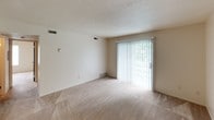 This single-floor unit features two bedrooms, one bathroom, and a well-organized layout designed for functional everyday living. The living area is carpeted in neutral tones and receives generous natural light through a sliding glass door dressed with vertical blinds, offering a view of green outdoor surroundings. A second set of sliding doors or a window in an adjacent space provides additional brightness, contributing to an open and airy feel throughout the common areas.

Both bedrooms are carpeted and feature windows with horizontal blinds that allow for controlled natural light. The neutral wall colors and textured ceilings maintain a consistent, understated aesthetic throughout.

The galley-style kitchen is lined on both sides with dark wood cabinetry offering ample storage, complemented by light countertops, a stainless steel sink, a gas range, and a full-size refrigerator. Tile flooring grounds the space practically. The bathroom includes a full tub and shower combination with chrome fixtures, a vanity with sink, and a medicine cabinet mirror, all finished in clean, neutral tones. Overall, the unit presents a straightforward, move-in-ready layout.