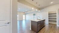 This well-designed single-story residence offers two bedrooms and two bathrooms within a thoughtfully arranged floor plan. The open-concept kitchen and living area serves as the heart of the home, highlighted by soaring ceilings that amplify the sense of space. The kitchen is outfitted with dark espresso cabinetry, stainless steel appliances including a refrigerator, range, and microwave, and a generously sized island topped with light quartz countertops. Pendant lighting hangs above the island, adding a modern touch. A dedicated pantry with built-in shelving provides ample storage directly off the kitchen.

The living area features light wood-look flooring and large windows that draw in abundant natural light. A glass door leads to an outdoor balcony, extending the living space and offering exterior views. Both bedrooms are finished with plush carpet flooring. The primary bedroom is a comfortable size and is accompanied by a walk-in closet with a built-in hanging rod and shelving. The bathrooms include a clean, white walk-in shower with built-in corner shelving. Neutral-toned walls throughout create a cohesive and move-in-ready aesthetic.
