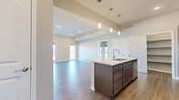 This well-designed single-story residence offers two bedrooms and two bathrooms within a thoughtfully arranged floor plan. The open-concept kitchen and living area serves as the heart of the home, highlighted by soaring ceilings that amplify the sense of space. The kitchen is outfitted with dark espresso cabinetry, stainless steel appliances including a refrigerator, range, and microwave, and a generously sized island topped with light quartz countertops. Pendant lighting hangs above the island, adding a modern touch. A dedicated pantry with built-in shelving provides ample storage directly off the kitchen.

The living area features light wood-look flooring and large windows that draw in abundant natural light. A glass door leads to an outdoor balcony, extending the living space and offering exterior views. Both bedrooms are finished with plush carpet flooring. The primary bedroom is a comfortable size and is accompanied by a walk-in closet with a built-in hanging rod and shelving. The bathrooms include a clean, white walk-in shower with built-in corner shelving. Neutral-toned walls throughout create a cohesive and move-in-ready aesthetic.